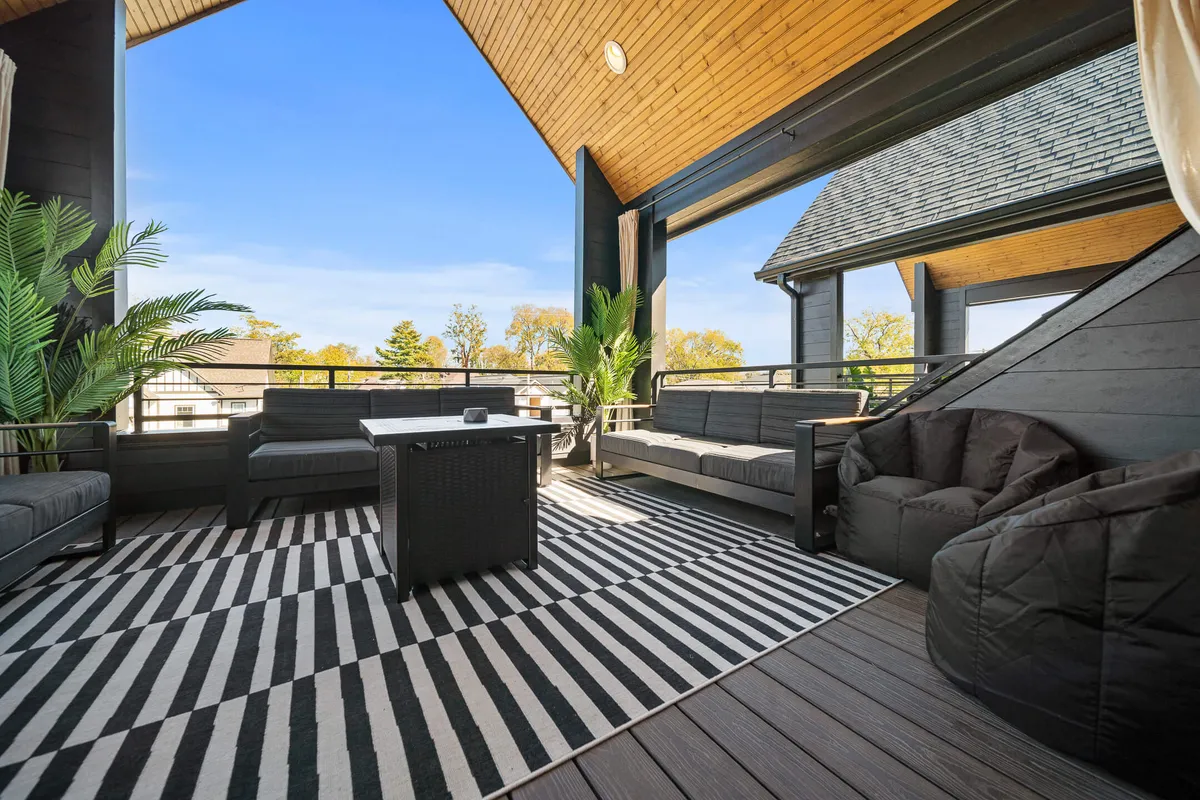 A modern exterior seating area with a black and white striped rug, contemporary furniture, and lush green plants. The layout is designed for comfort and sociability, ideal for mingling, enjoying cocktails, or relaxing outdoors during a celebration. The atmosphere is inviting and sophisticated, well-suited for upscale rooftop gatherings.