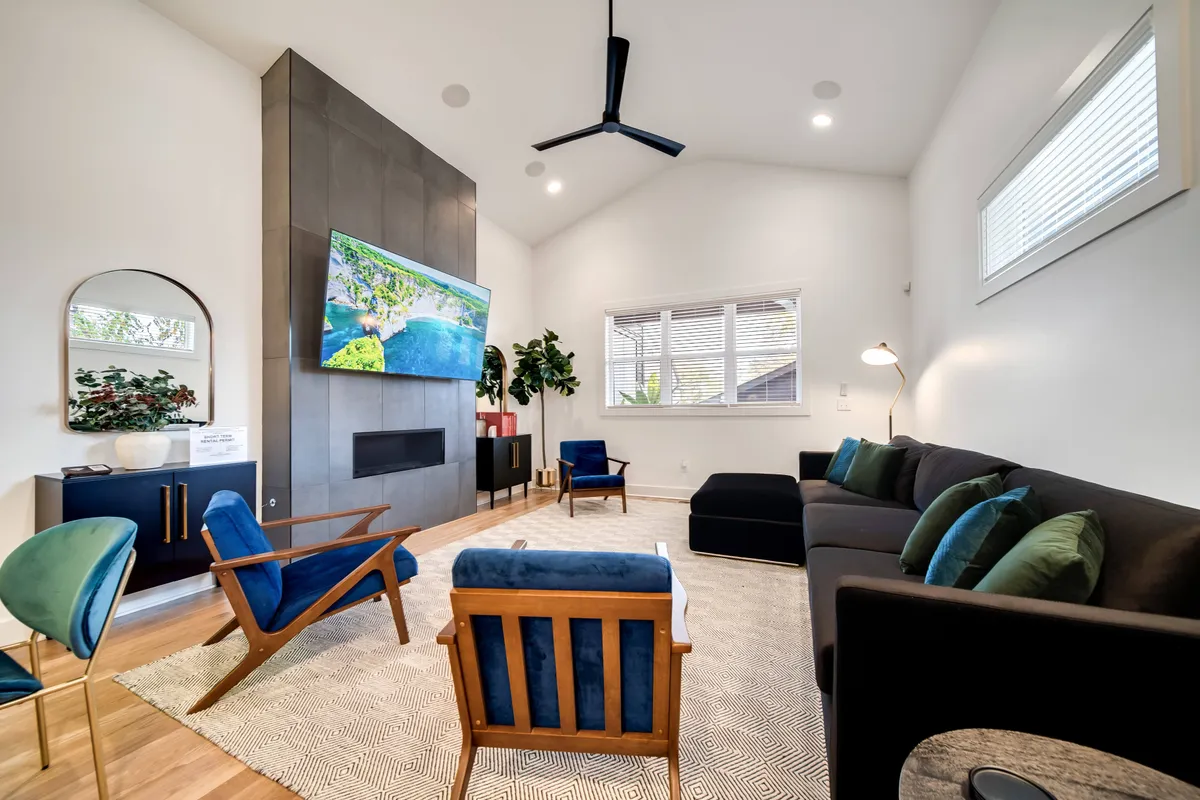 A contemporary living area with a modern fireplace, large TV displaying a calming nature scene, and stylish seating arrangements. Natural light streams in, creating a cozy yet open and sociable atmosphere.