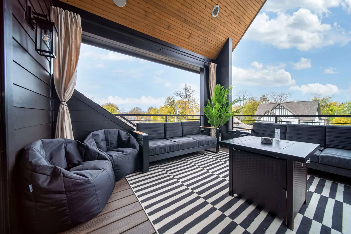 A stylish outdoor seating area featuring black furniture, a striped rug, and lush plant accents. The space is positioned to maximize views of the surrounding landscape, perfect for socializing, sipping drinks, or savoring quiet moments after an evening out.