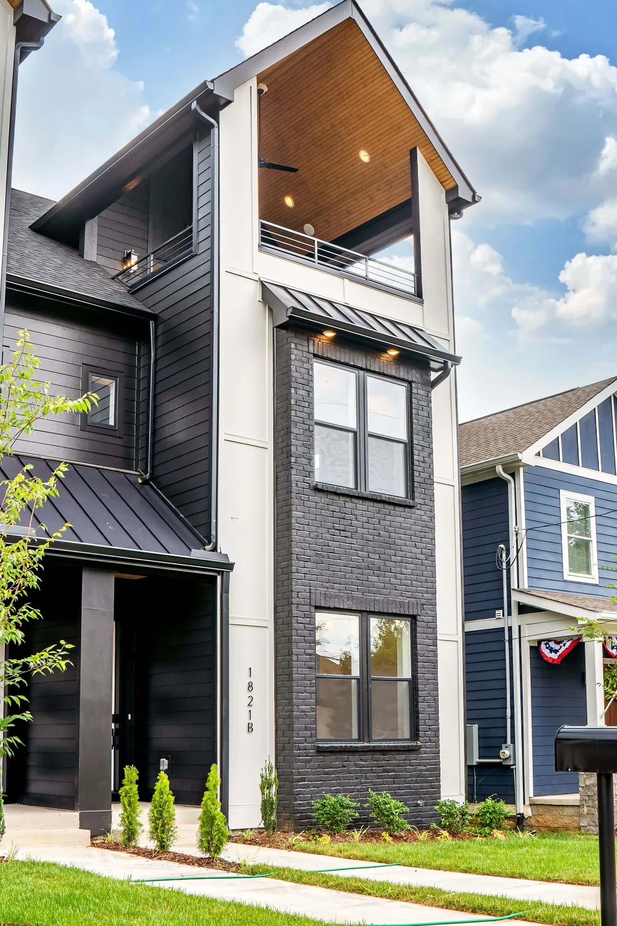 This exterior image showcases modern architecture with a striking contrast between black brick and lighter siding. The view includes an outdoor balcony, hinting at a private rooftop space suitable for relaxing or entertaining. The welcoming, contemporary mood sets the stage for an upscale Nashville adventure.