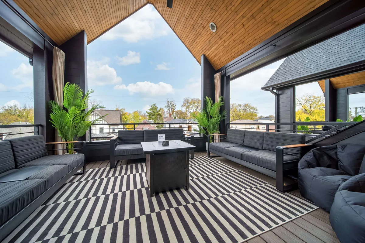 An outdoor rooftop lounge area featuring a stylish arrangement of seating with decorative plants, a visually striking striped rug, and sweeping views of the surrounding area. The ambiance evokes comfort and sociability, ideal for gathering under the open sky. The scene is set at sunset, adding to the allure and exclusivity of the space.