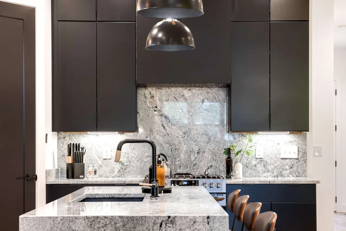 Featuring granite countertops, black cabinetry, modern pendant lights, and stainless steel appliances, this kitchen offers a sophisticated yet inviting space for cooking and entertaining. The layout is open and functional, ideal for both everyday use and special occasions.