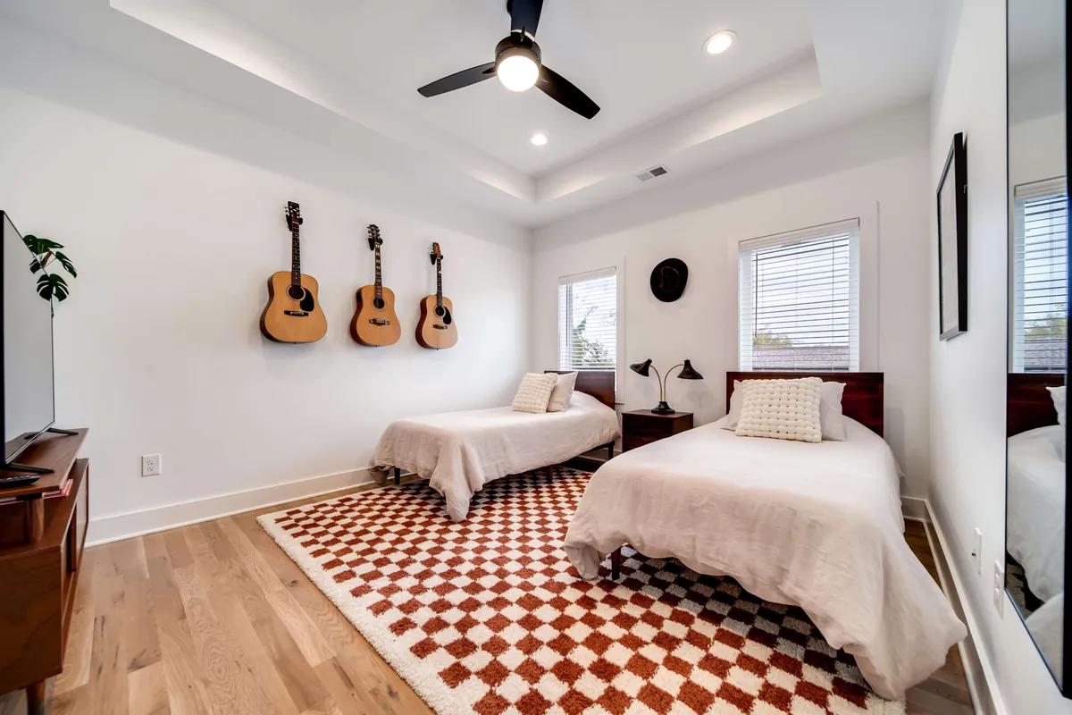 An artistic bedroom with guitars displayed on the wall, a cozy bed arrangement, patterned rug, and large windows providing ample natural light. The setting encourages music-making, reading, or spontaneous conversations, reflecting Nashville's cultural vibe within the home.