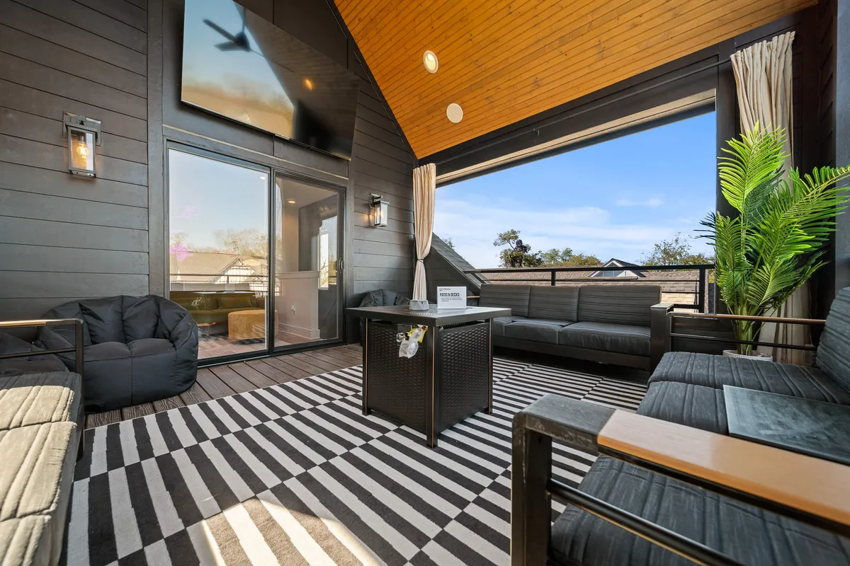 A bright, open-concept living space featuring a large TV, comfortable seating, a striped rug, and a potted plant beside wide windows. The arrangement invites group gatherings for socializing or enjoying movies together, with views suggesting connection to the outdoors.