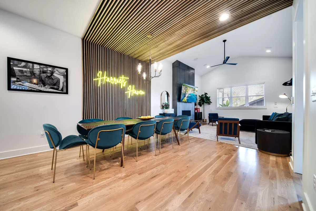 The image showcases a sleek and spacious dining area with a modern table set for a gathering, accented by vibrant artwork and a playful neon sign. The open living area features a cozy couch, inviting conversation and relaxation, while the décor effortlessly blends mid-century modern flair with artistic touches, creating an atmosphere perfect for entertaining or unwinding.